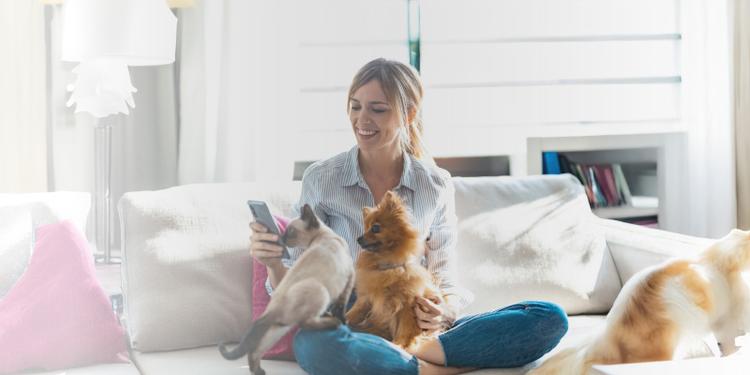 a woman holding her dog and cat while checking her phone